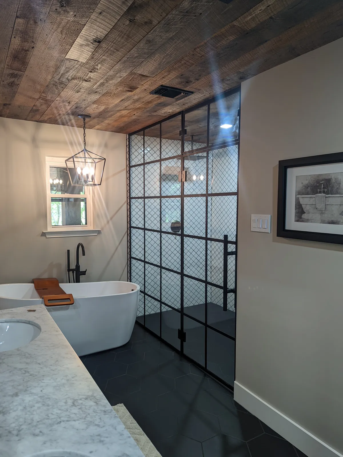 Black grid glass panel beside a freestanding tub under a wood plank ceiling