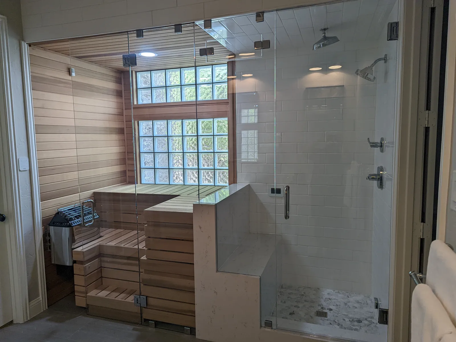 Floor-to-ceiling glass enclosure in front of a steam shower and a wood-lined sauna
